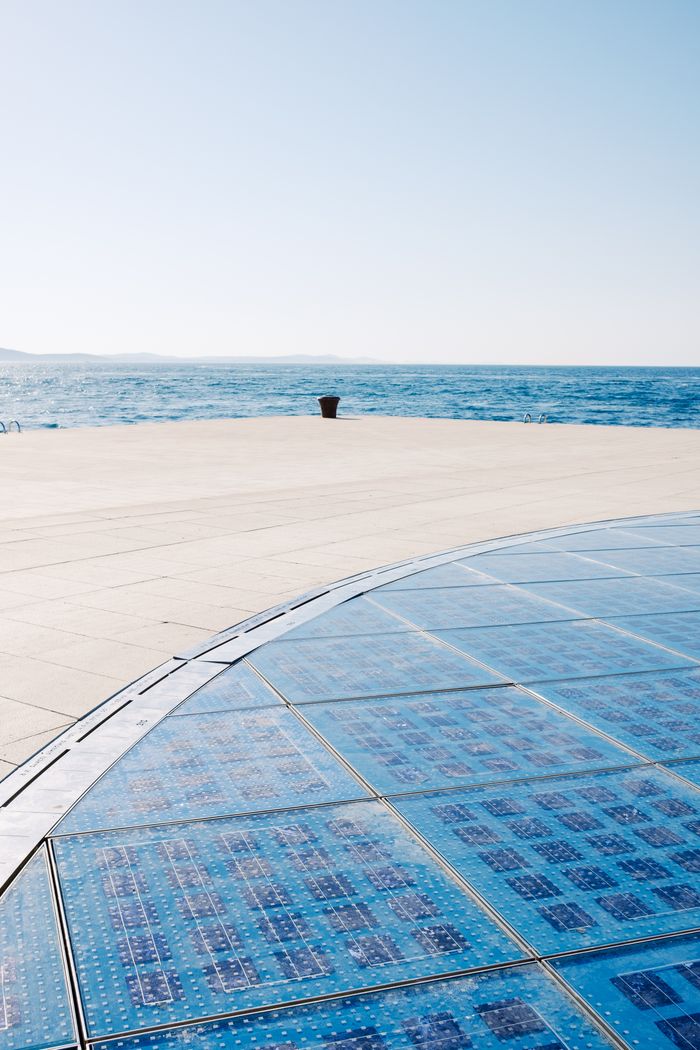 Wide view of solar panel installation near ocean under clear sky.